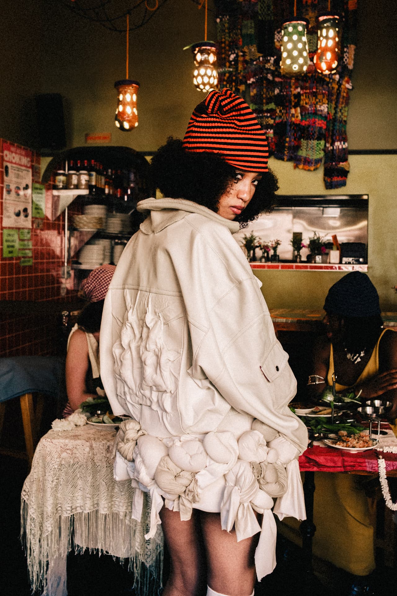 Model in a sculpted cream jacket with knotted jersey hem inside a Cambodian restaurant.